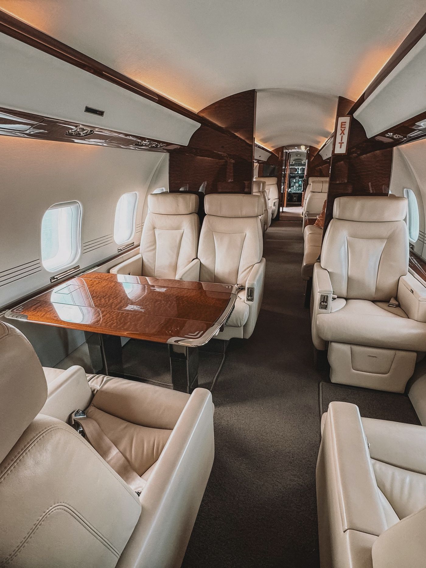 Business jet cabin with cream leather club seats and a wood-trimmed table