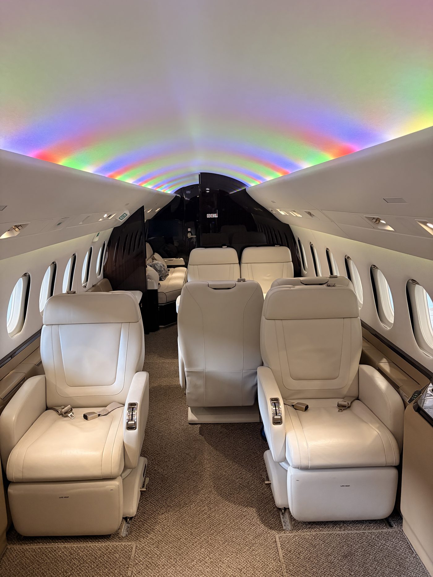 Business jet cabin with rainbow ceiling lighting over cream leather seats