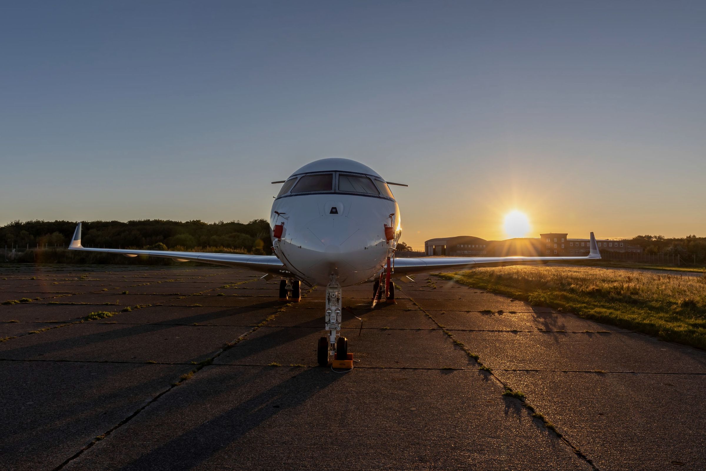 Business jet parked nose-on on a quiet ramp with the sun setting behind it